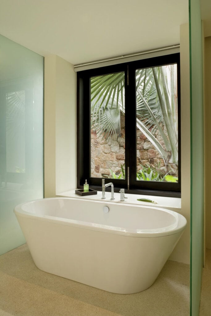 家里的一个有独立浸泡浴缸的浴室看起来在掌心。磨砂玻璃面板有助于保持溅到最低限度,并提供一个小的隐私。
