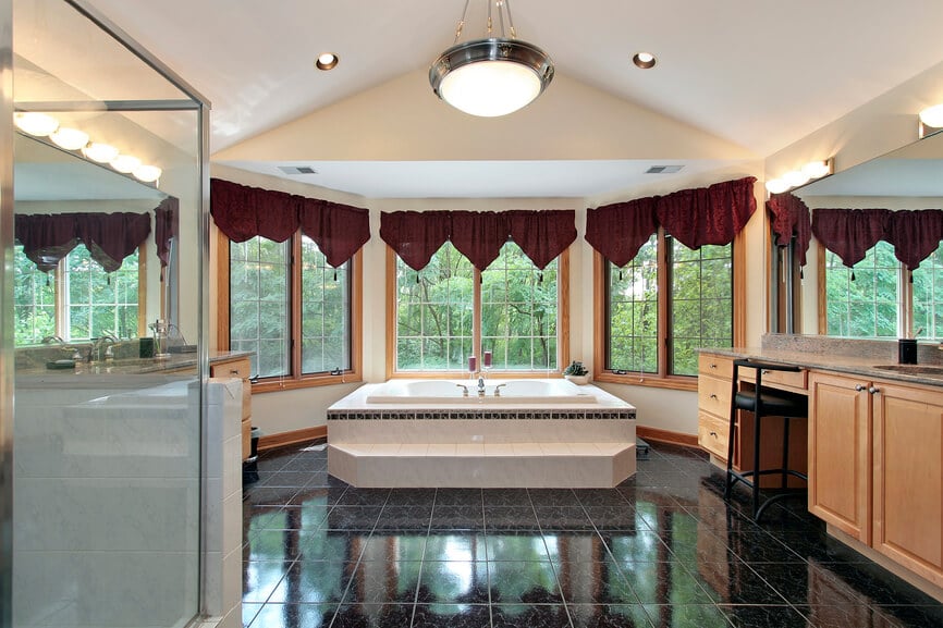 这间宽敞的拱形天花板浴室配有黑色瓷砖地板，一大片空间连接着一对功能齐全的梳妆台和一个大浴缸。一系列飘窗和丰富的天然硬木提供了广阔的视野和自然的触感。