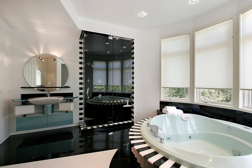 这个超现代的浴室以一系列圆形特征为特色，与尖锐的角度形成对比。黑色地板和淋浴室内与白色墙壁和独特的分段梳妆台设计形成鲜明对比。按摩浴缸以黑白条纹为框架。