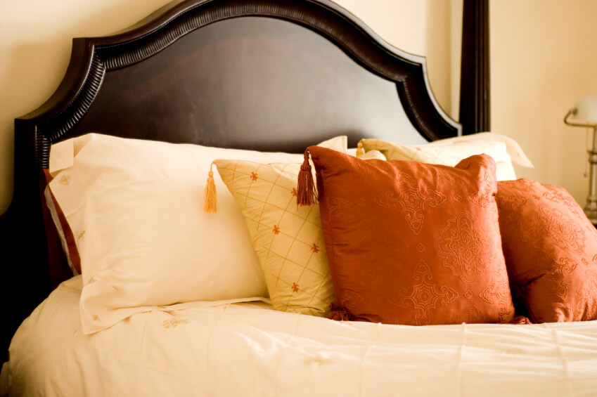 带有角落流苏的锈橙色和黄色枕头与精致刺绣的奶油色枕枕形成鲜明对比。深色床头板为额外的美丽和兴趣提供了最佳的对比。