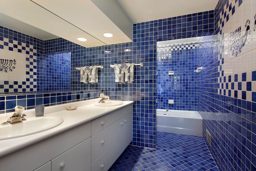 这是一个独特的浴室，即使在这个画廊里。大胆的蓝色瓷砖从地板上延伸到墙上，一直延伸到白色的天花板，包裹着一个大型的白色双梳妆台和浴缸。