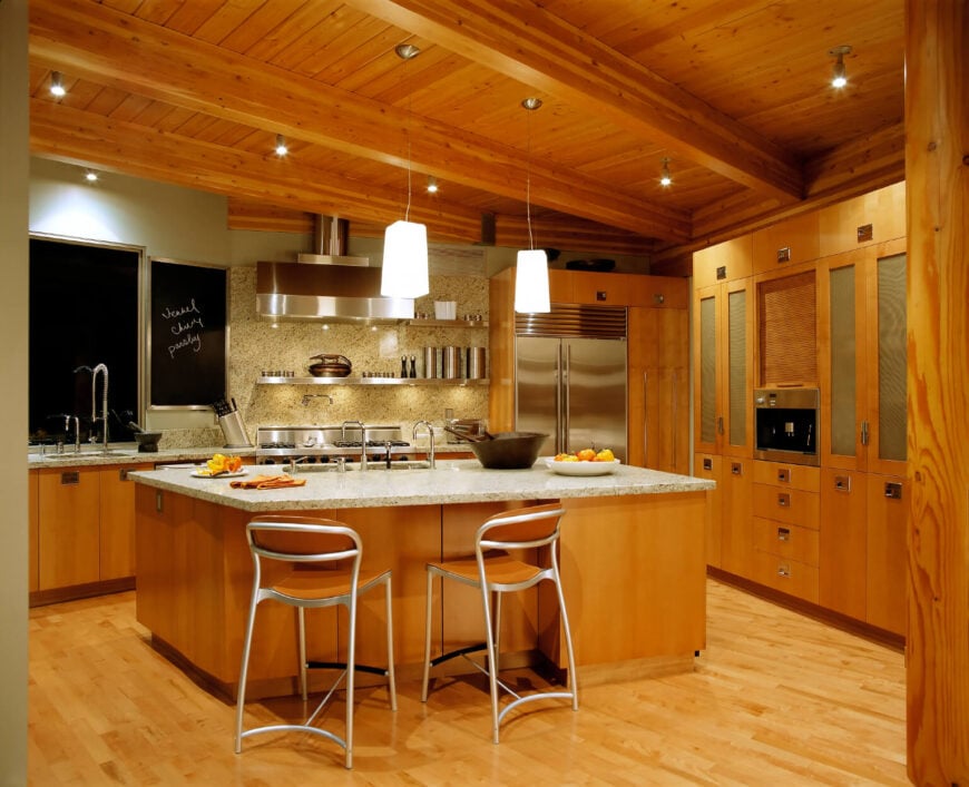 这间厨房温暖的蜂蜜色调与浅色花岗岩台面和配套的后挡板形成对比。墙壁上使用的黑板增加了功能性和趣味性。