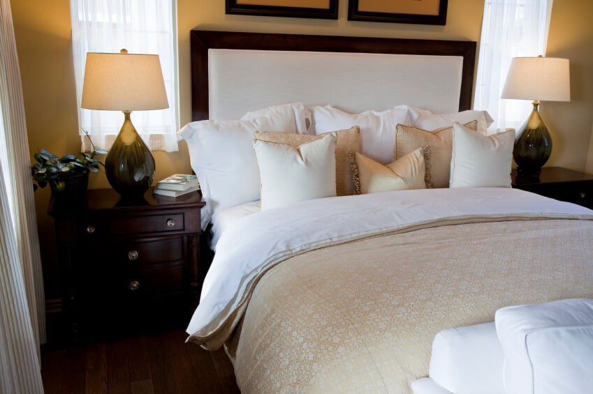 金色、白色和象牙色的色调被深而丰富的硬木家具所抵消。填充的床头板支撑着大量的强调枕头，与房间的其他部分完美地互补。
