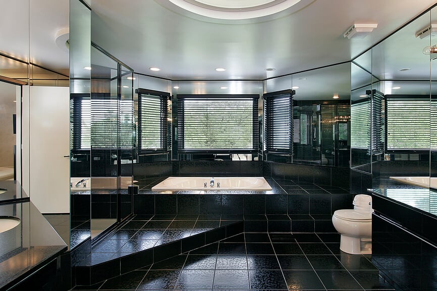 这个超豪华的浴室在黑色瓷砖地板的海洋上，每个垂直表面都有环绕式镜子。高低不一的楼层在一排窗户下面围起了一个浴缸。