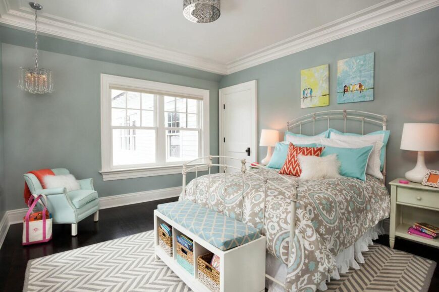 一间时尚的女性卧室，白色锻铁床架和灰色、浅蓝色和橙色的调色板。床后面的墙上有两幅小画。