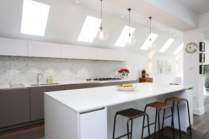 厨房的特点是在光滑的白色台面上安装了复杂的微型瓷砖后挡板，再加上岛台上方的三盏裸露的玻璃吊灯。