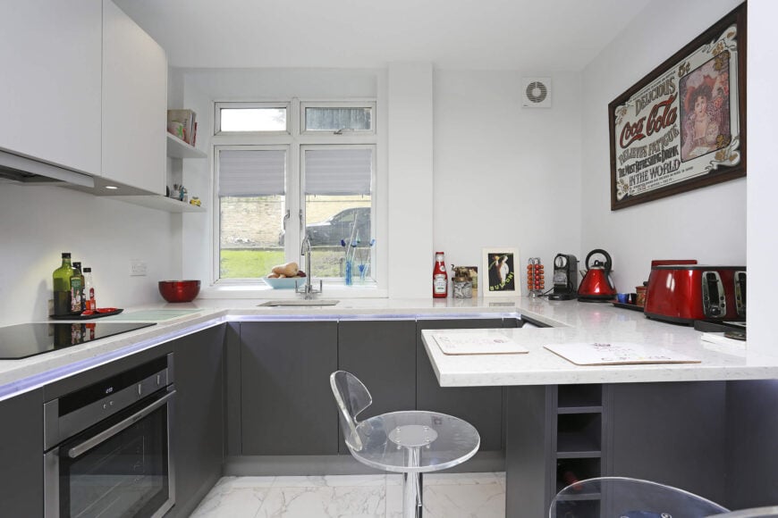 深灰色的下部橱柜和白色环境之间的强烈对比定义了这个舒适的厨房。u形台面设有一个小半岛，可用于用餐或学习空间。
