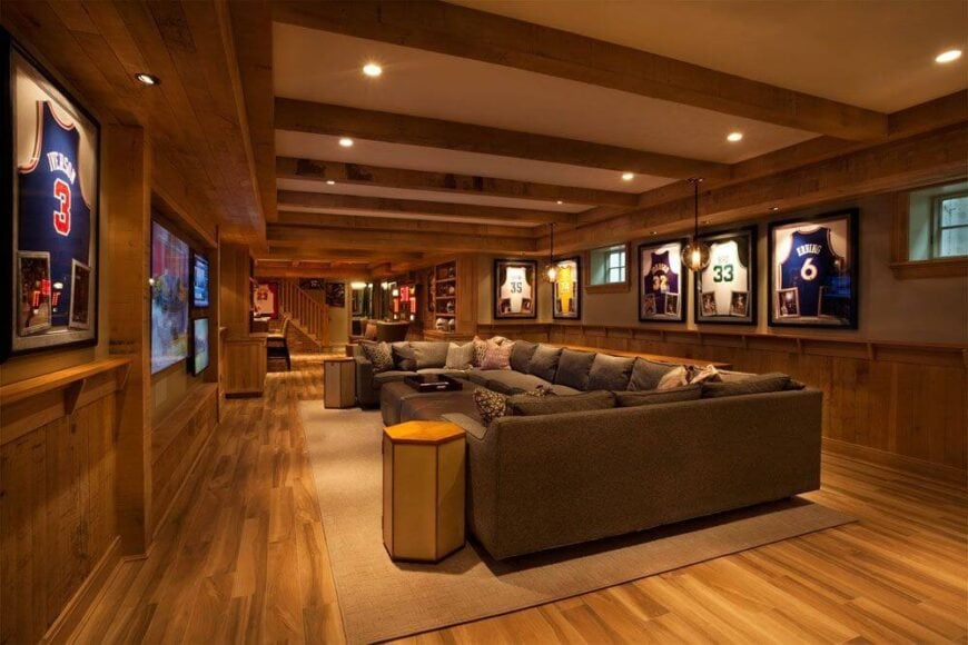 房间的另一侧是宽敞的家庭娱乐室，里面有一张巨大的u型组合沙发，上面有几张奥斯曼沙发。墙上装饰着镶框的运动衫。左边的墙上有一个大电视，旁边有两个小电视，可以提供最佳的观赛体验。