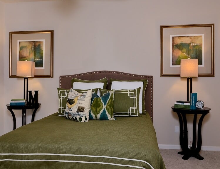 这个定制的卧室以绿色床上用品后面的丰富的皮革床头板为特色，两侧是一对带有互补灯的黑色边桌。配套的画作悬挂在上方。