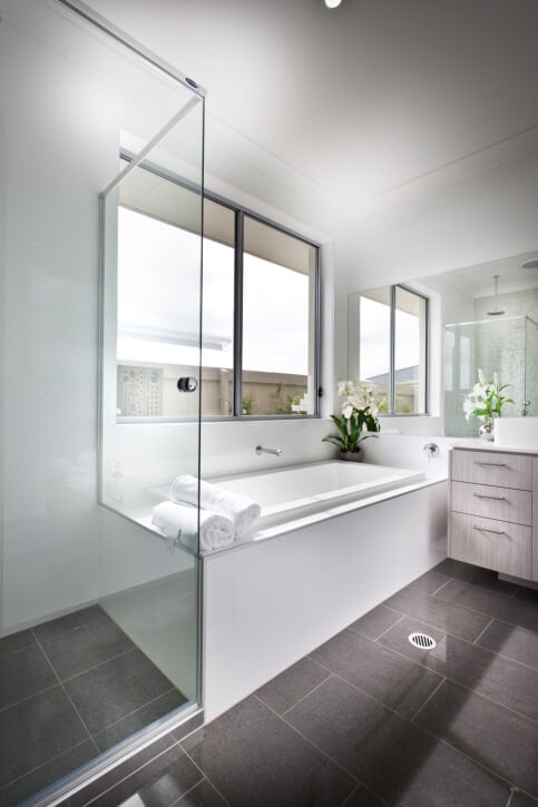 这间明亮的浴室设有大型棕色瓷砖地板和白色墙壁和浴室环绕。梳妆台上的轻木橱柜增加了一层细节，玻璃封闭的淋浴间也是如此。