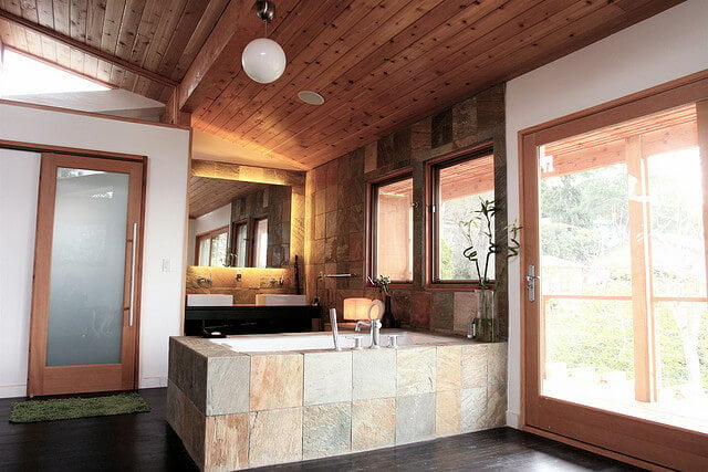 这个浴室混合了现代和乡村元素，为一个独特的外观。深色硬木地板、石砖环绕浴缸和明亮的天然木镶板创造了有趣的纹理组合。