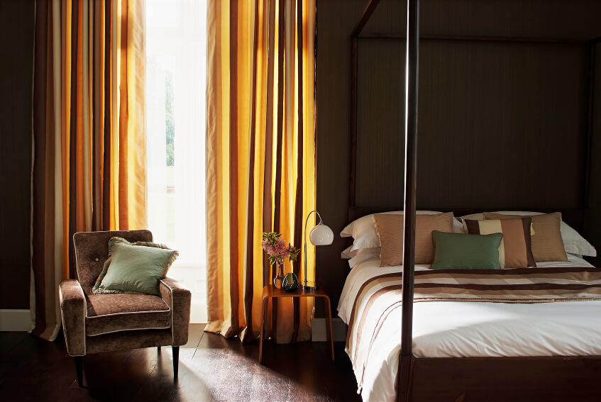 这间卧室以精致的金色窗帘为特色，自然光线透过织物而发光。一张柔软的扶手椅放在四柱床旁边，床上装饰着金色、绿色、象牙色和棕色，将整个空间联系在一起，产生令人惊叹的效果。