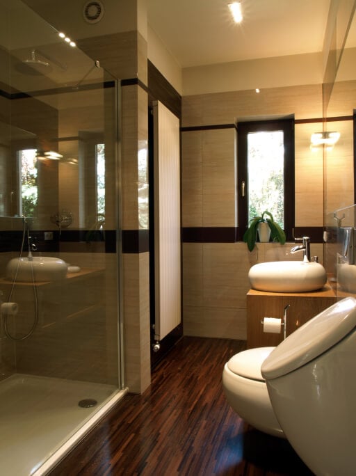 这间纹理丰富的浴室以深色、丰富色调的细板硬木地板为特色，在纹理米色的墙壁下，还有带容器水槽的浅色木质梳妆台。玻璃封闭淋浴和现代化的便利设施创造了新鲜的外观。
