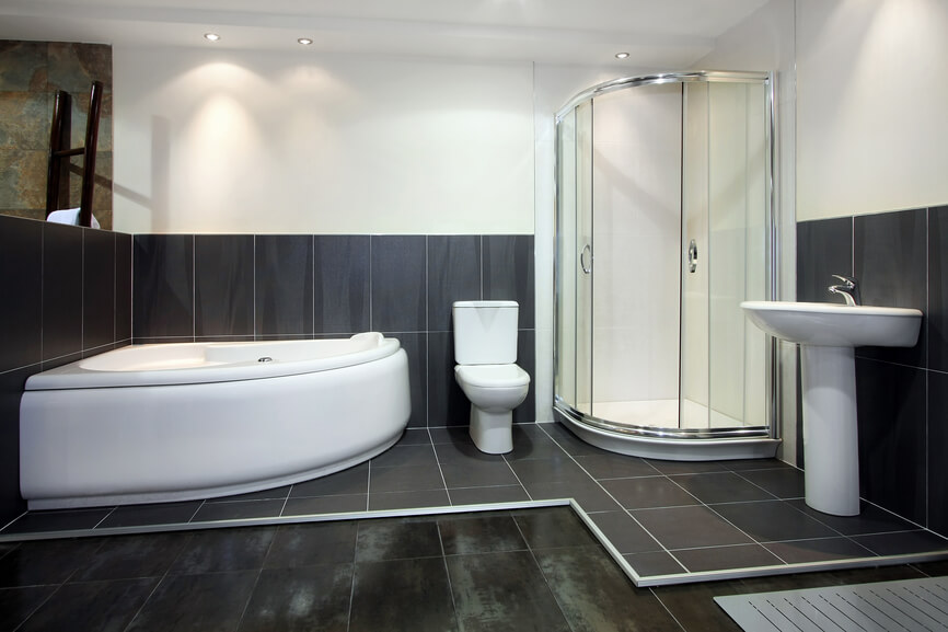这个高对比度的浴室以大面积磨损的黑色地砖和围绕浴室区域的凸起黑色瓷砖表面为特色。弧形玻璃封闭的淋浴间填满了角落，与角落安装的白色浸泡浴缸相对。