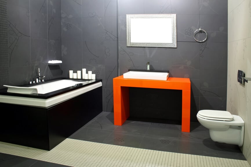 这间超现代的浴室以深灰色地板和墙壁上的色彩爆发为特色，中间有一个橙色的梳妆台。大型浴缸是黑白框，进一步的对比和细节。