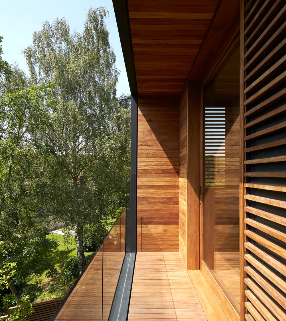 阳台以其丰富的天然木框架，与无框玻璃安全墙和周围的绿色环境并置。
