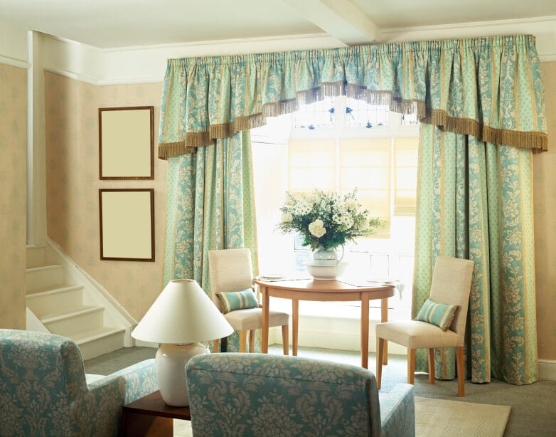 浅蓝色厚重的传统窗帘架在凸窗上，后面是一张小桌子和几把没有扶手的椅子。