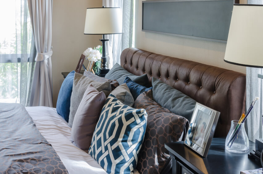互补的蓝色、棕色和灰色给这个房间一个舒适的空气和经典的感觉。长毛绒皮革床头板上摆放着各种各样的抱枕，创造了一个令人赏心悦目的温馨舒适的空间。