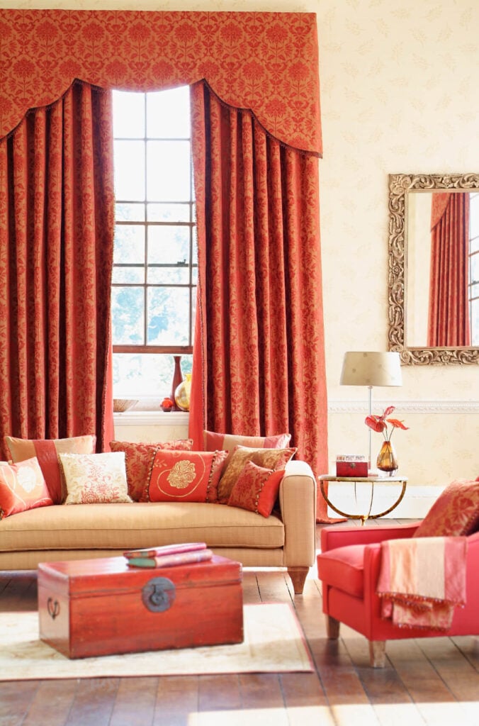 红色锦缎窗帘与橙红色的家具相得益彰。一面镀金的镜子增加了房间的奢华感。