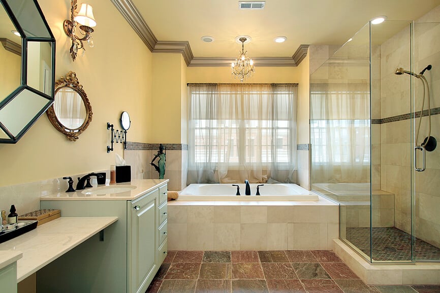 这间主浴室以丰富的大地色调瓷砖地板为特色，带有深红和绿色色调，将充满大理石和柔和黄色色调的空间结合在一起。右侧的全玻璃淋浴房拥抱着大型浸泡浴缸，而左侧的双梳妆台则采用柔和的绿色涂漆橱柜。