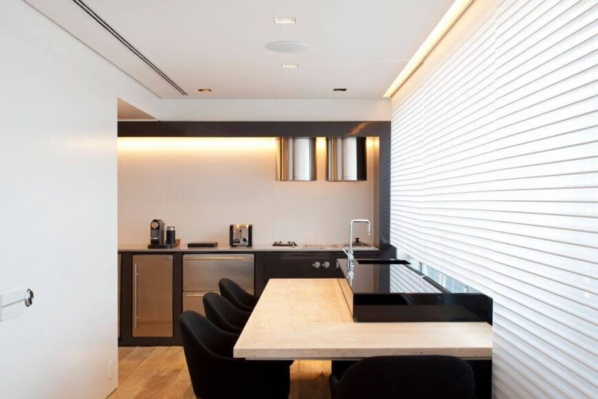 厨房特写，展示了一个两层的餐厅吧台和简单、低调的不锈钢用具。厚重的白色窗帘可以升起，以便从宽敞的窗户中获得更多的自然光线。