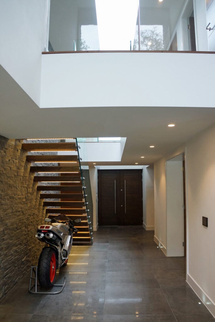 这条走廊用嵌入式照明和浮动楼梯上的条形灯照明，那里停放着一辆摩托车。