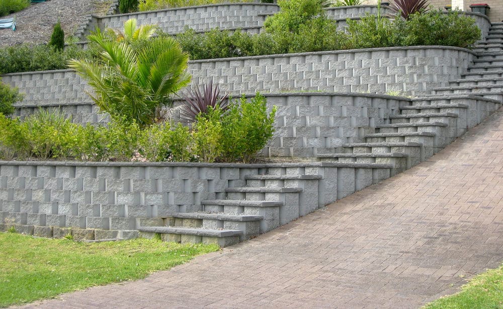 多层砖挡土墙展示了令人惊叹的3d设计和侧面的匹配楼梯。统一的灰色使绿色植物格外突出。