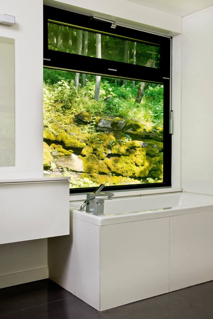 较低的浴室从浴缸可以看到山景。大面积深色瓷砖地板与纯净的白色台面和墙壁形成对比。
