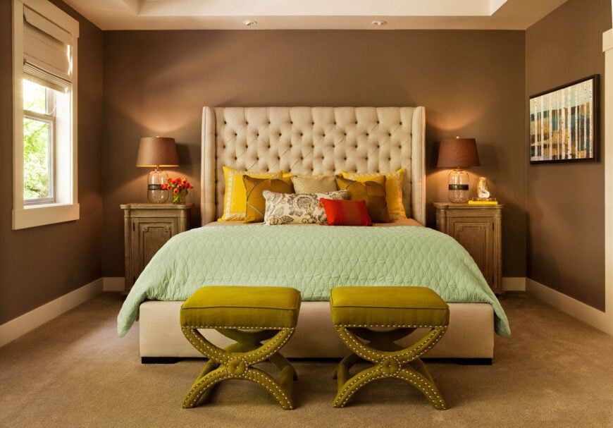 主卧室包含了一个独特的家庭颜色主题的变化，一个充满活力的米色纽扣簇床头板站在摩卡棕色的墙壁上，深色米色地毯。床的两侧放着一对质朴的木边桌。