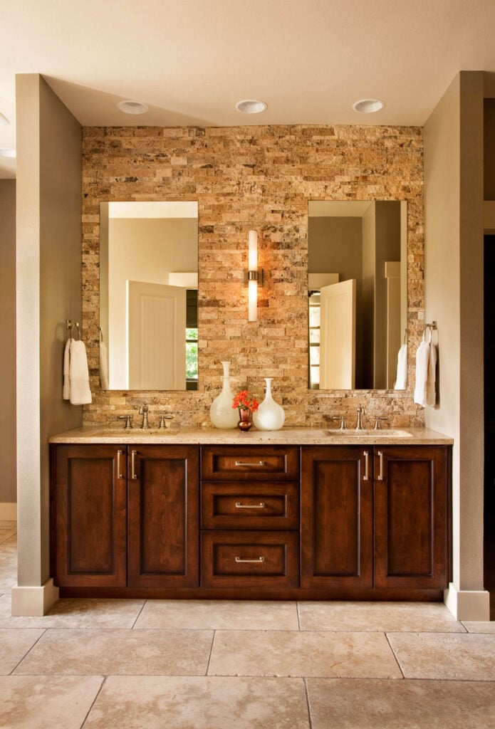 主浴室里的木质双梳妆台顶部是花岗岩台面，无框镜子挂在上面的石砖墙上。