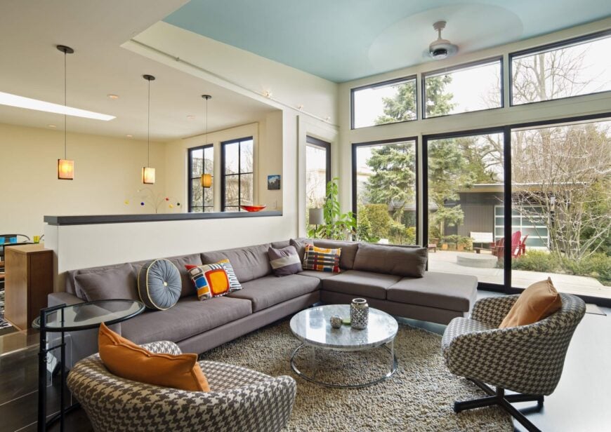 客厅通过通高的窗户沐浴在阳光下，有一对现代扶手椅和一条长长的现代组合沙发共用一块区域地毯。