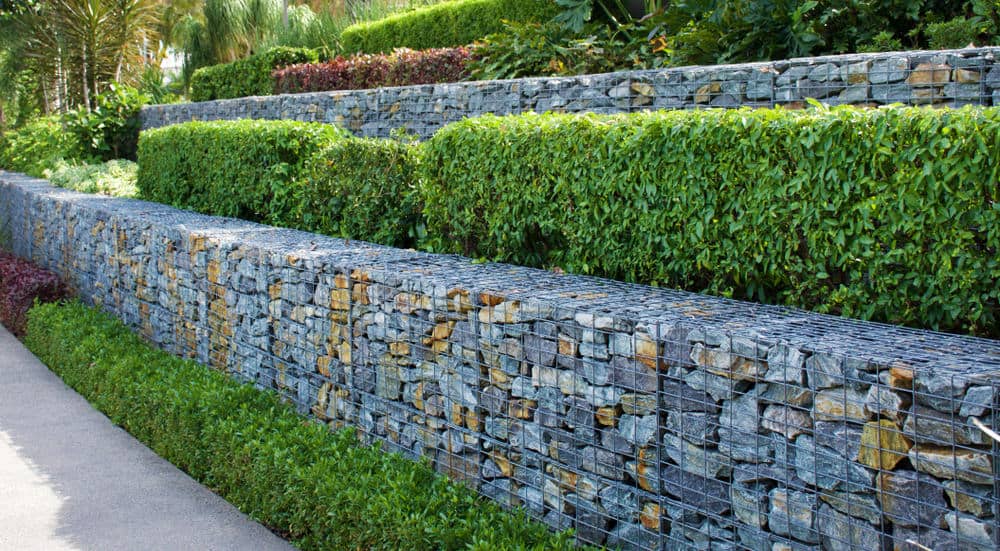 两种色调的多层石笼挡土墙伴随着交替修剪的植物，在后院创造了一个令人惊叹的栅栏。