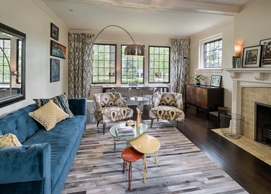 这个更正式的客厅，以右边的一个大壁炉为中心，可以看到迷人的纹理混合。条纹地毯铺在厚实的硬木地板上，上面放着一张长长的蓝色沙发和一对扶手椅，还有三色的咖啡桌。