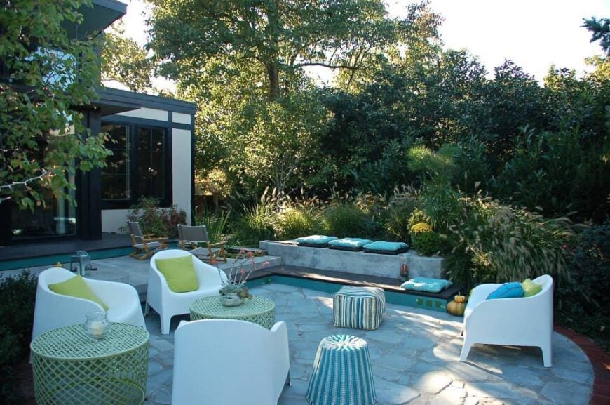 后院有许多独特的座位选择，白色扶手椅和柳条桌子坐落在房子后面郁郁葱葱的绿色植物中。