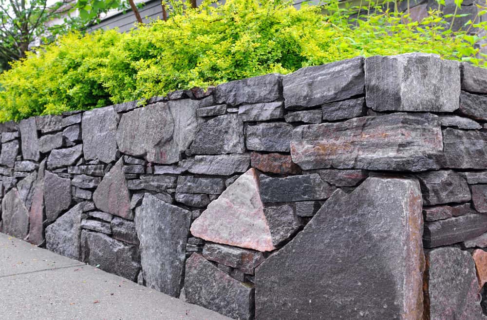 独特的岩石挡土墙由各种形状和大小的人行道组成，创造了一个有趣的外观。它的顶部是常绿植物，给墙壁带来了生命。