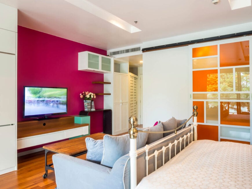 这是一间现代风格的卧室，将浆果色和橙色等当代大胆的色彩与复古家具结合在一起，白色锻铁床架底部有一张浅蓝色沙发。