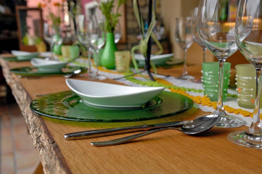 一个宽大的绿色玻璃餐盘上放着一个细长的汤碗。右边是两个大酒杯，在餐具的上面。