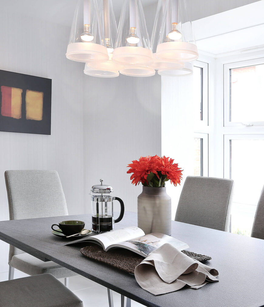 餐厅空间位于住宅的主要开放式区域内，以中性灰色和白色为主色调，中间有一张花岗岩台面的极简主义桌子。桌子两侧是浅灰色的帕森(Parson)椅子，下面是一组锥形的玻璃吊灯。
