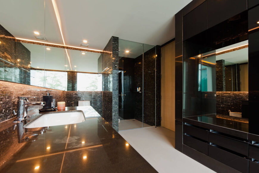 主浴室与房屋的其他部分形成鲜明对比，装饰着丰富的黑色瓷砖，夹在白色地板和天花板之间。一个微型瓷砖后挡板通向封闭式的步入式淋浴间。