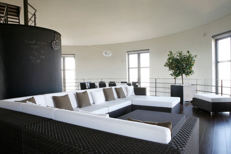 在黑板楼梯的对面是一个巨大的黑色柳条组合家具，上面有原始的白色靠垫和暗灰褐色的枕头。软脚凳可以靠在躺椅上，也可以用作额外的座位
