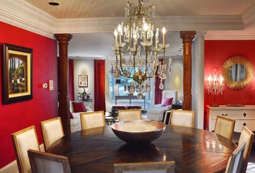 餐厅俯瞰着客厅，有一个宽阔的开口，两侧有硬木柱子。巨大的圆形桌子可容纳10人，与大胆的红色墙壁色调和整个空间的华丽细节形成鲜明对比。