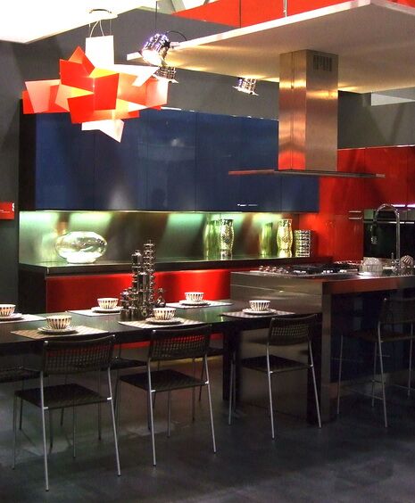 这个独特的厨房充满了大胆的红色和蓝色。与现代吊灯一样，橱柜下的照明也会产生温暖的光芒。