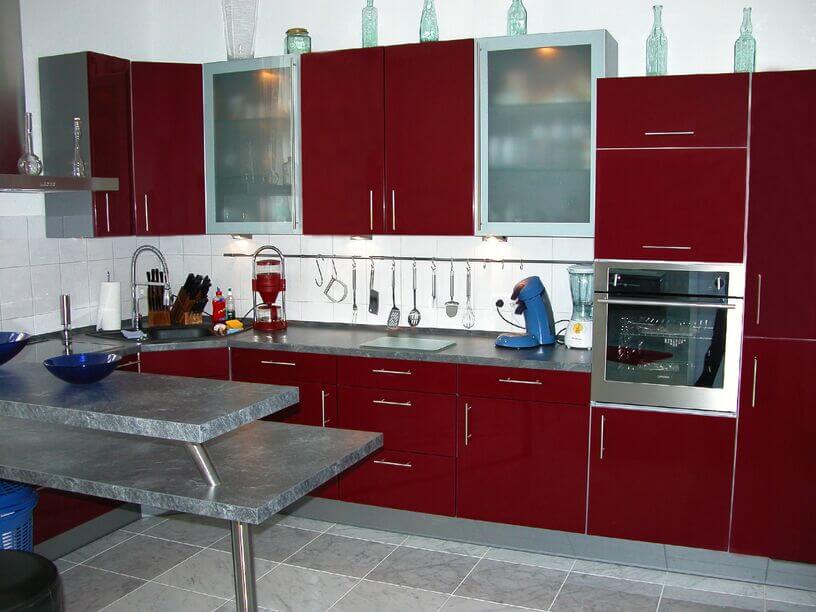 这间灰白色的厨房以深红的橱柜为特色。丰富的色调与地板和后挡板上的浅色形成了鲜明的对比。