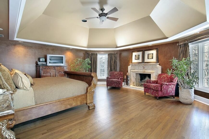 高耸的天花板在上面的设计中是一个真正的亮点。它骄傲地漂浮在蜂蜜色的硬木地板上，一张漂亮的雪橇式床，上面装饰着米色的中性亚麻制品，洋红色和米色的图案突出的椅子，还有一个美丽的壁炉。墙壁的纹理使人想起床上的木制品。一台平板电视安置在一个协调的支架上，从床和椅子上都能看到。