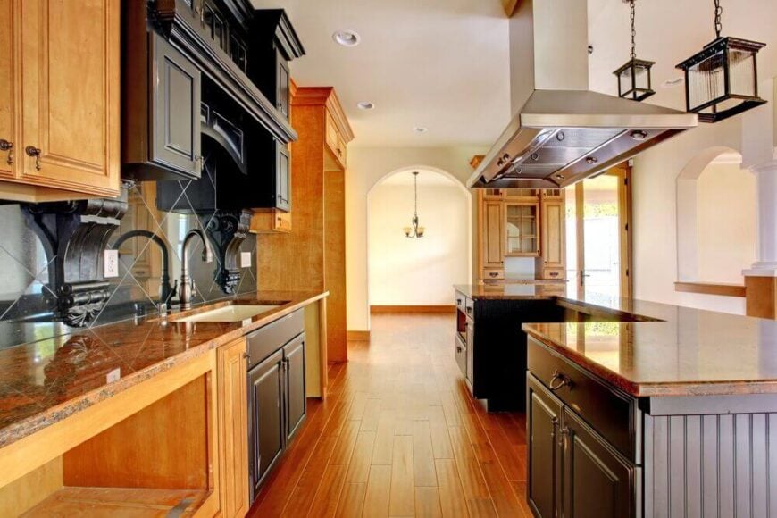 这个漫长的厨房从地板到地面都洋溢着温暖的自然木材色调。巨大的u形岛在右边设有一个腔放置一个全尺寸的炉子和范围，正下方的大型不锈钢罩通风口。