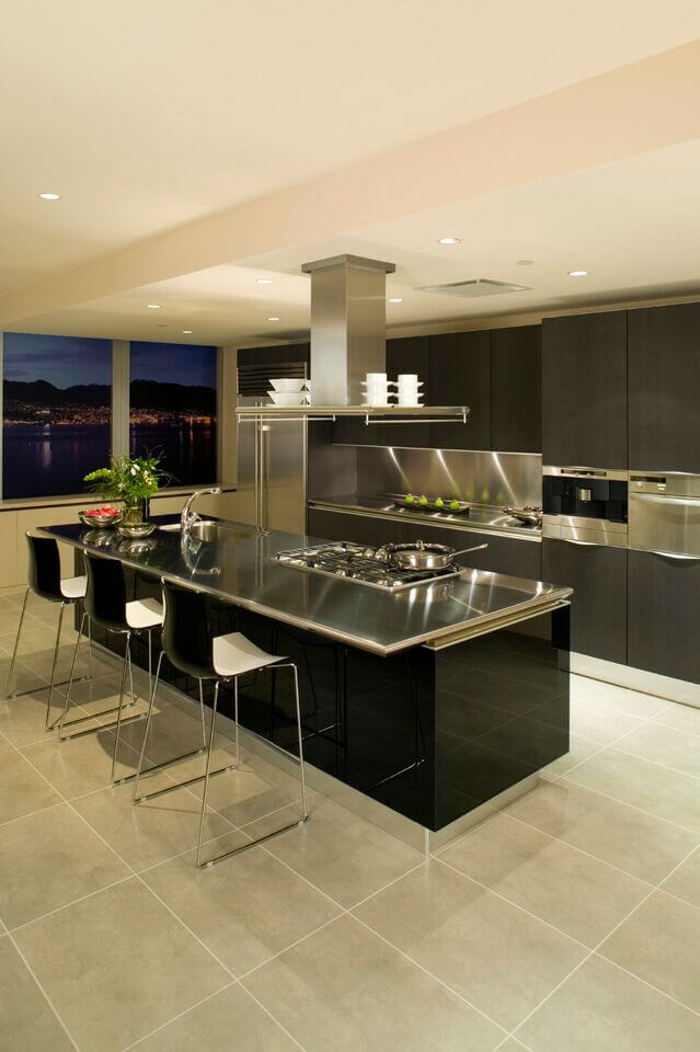 在一个超现代的厨房里，拥有不锈钢台面和大面积瓷砖地板，黑色的长岛设有一个大型煤气灶和完整的内置水槽。深色染色的极简主义橱柜使画面更加完美。