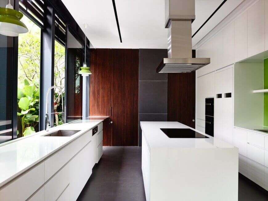 在另一个极简主义和现代厨房里，我们看到了丰富的纹理，包括光滑的白色橱柜和台面，木炭瓷砖地板，以及远处墙壁上丰富的木材细节。白色岛的特点是光滑的黑色灶台下不锈钢罩通风口。