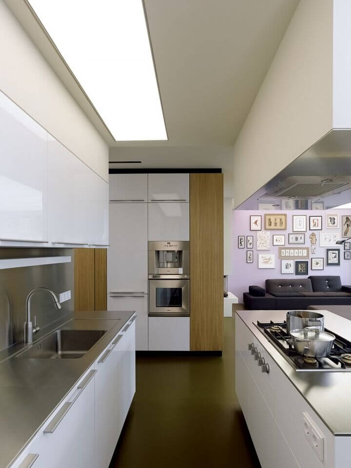 在一个开放式的住宅中，中心有一个厨房，岛屿定义了这个空间。不锈钢台面与白色橱柜和天然木墙细节形成鲜明对比，岛上有谨慎的煤气灶顶部，表盘正好嵌入壁板。