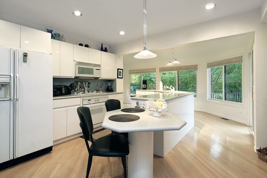 在这个明亮而现代的厨房里，我们看到了一个独特的岛式设计。l型的岛屿与众不同，有一个内置的水槽和丰富的储物空间，还有一个附属的高餐桌。蛇形设计有助于定义厨房空间，同时加强大胆的白色调色板。