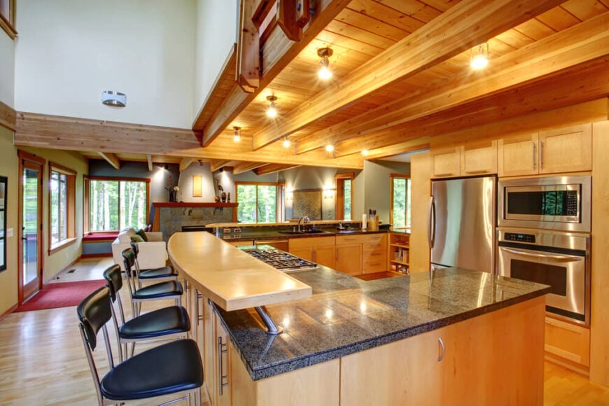 这个厨房有着现代的乡村风格和开放式设计，从地板到天花板都是丰富的天然木材色调。裸露的木梁与橱柜和硬木地板相匹配，而l形的岛屿本身拥有一个上层的轻木餐厅层。巨大的花岗岩台面包括一个煤气灶和充足的工作空间。